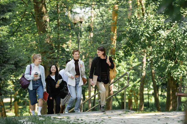 Positive students with backpacks walking with friends in park