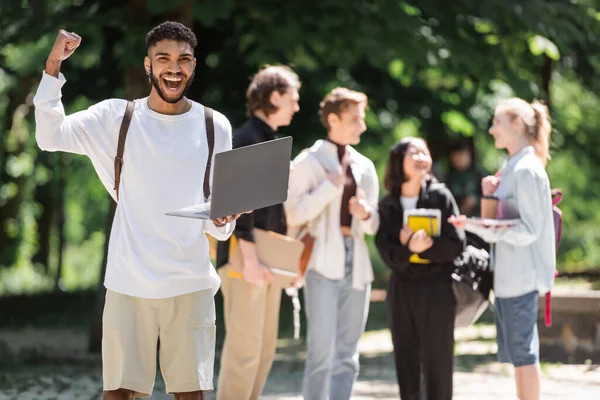 Emocionado Estudiante Afroamericano Sosteniendo Portátil Cerca Amigos Borrosos Parque — Foto de Stock