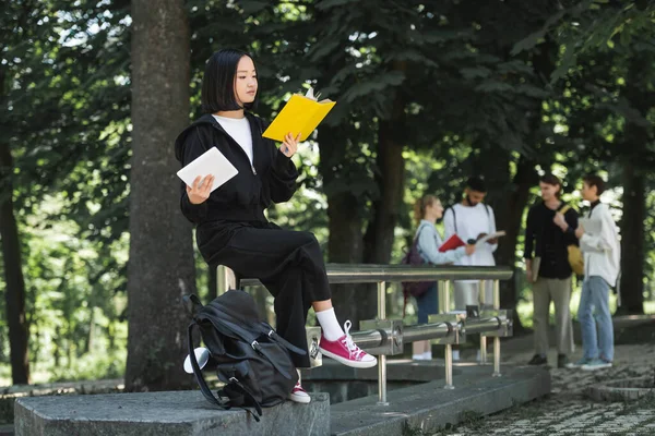 Asian Student Reading Book Holding Digital Tablet Park — Fotografia de Stock