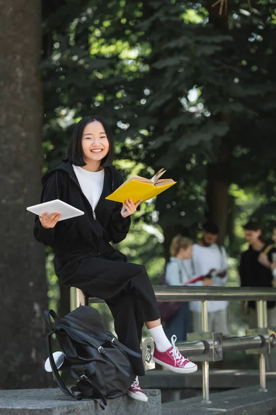 Cheerful Asian Student Book Digital Tablet Looking Camera Backpack Park — Foto Stock