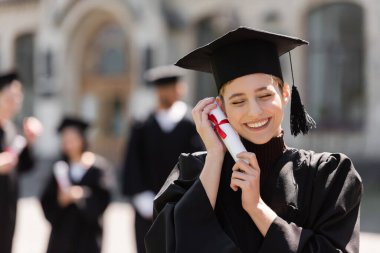 Kapüşonlu neşeli bekar diplomasını açık havada tutuyor. 