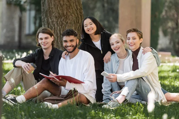 Cheerful Interracial Students Cellphone Copy Book Looking Camera Park — Zdjęcie stockowe