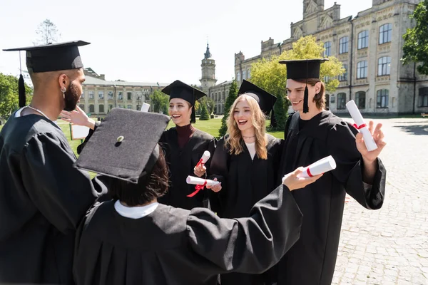 Positive Multiethnic Bachelors Caps Gowns Holding Diplomas Park — Stock fotografie