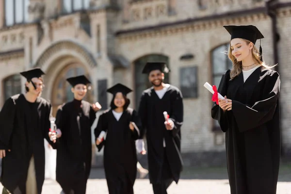 Smiling Bachelor Looking Diploma Blurred Multiethnic Friends University Outdoors — Stock Photo, Image