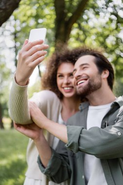 happy young couple taking selfie on smartphone in green summer park 