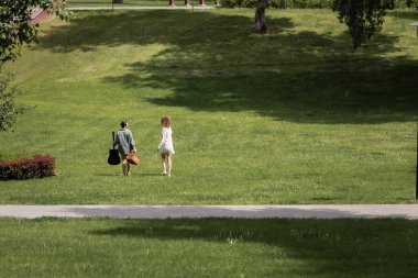 full length of man in summer clothes carrying guitar and picnic wicker basket near girlfriend in green park 
