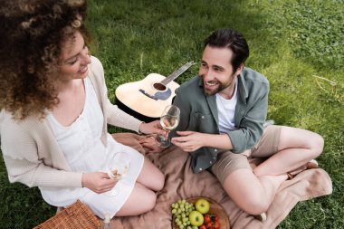 high angle view of happy curly woman passing glass of wine to boyfriend during summer picnic
