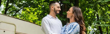 bearded gay man looking at happy boyfriend near travel van, banner