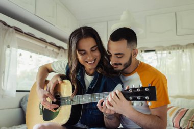 Gülümseyen, uzun saçlı, akustik gitar çalan, modern minibüste mutlu bir erkek arkadaş. 