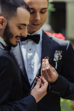 happy gay couple in formal wear holding wedding rings in hands 