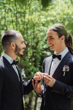 side view of happy gay man wearing wedding ring on finger of cheerful groom 