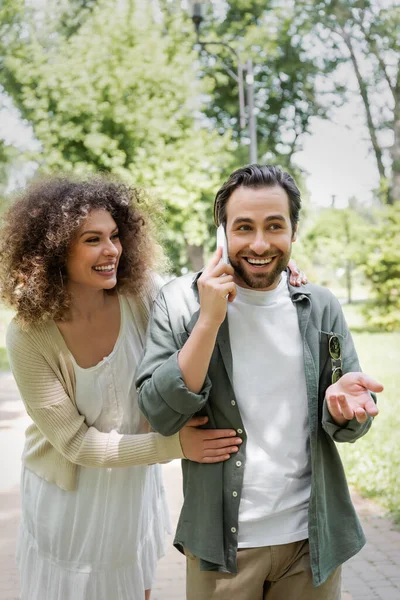 Mujer Rizada Abrazando Novio Alegre Hablando Teléfono Inteligente Parque Verde —  Fotos de Stock