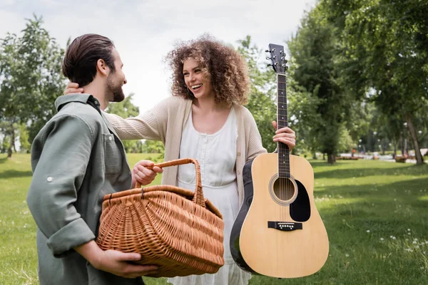 Happy Curly Woman Holding Acoustic Guitar Hugging Boyfriend Wicker Basket — Foto de Stock