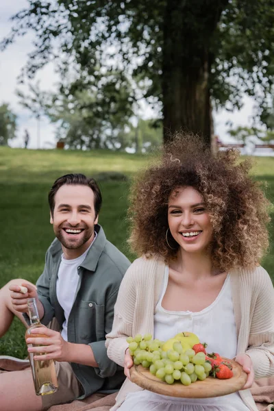 Happy Man Opening Bottle Wine Smiling Curly Girlfriend Sitting Fruits — Foto de Stock