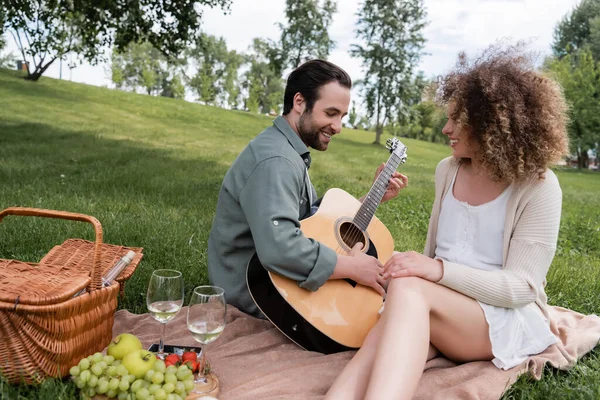 Hombre Feliz Tocando Guitarra Acústica Cerca Mujer Rizada Durante Picnic —  Fotos de Stock