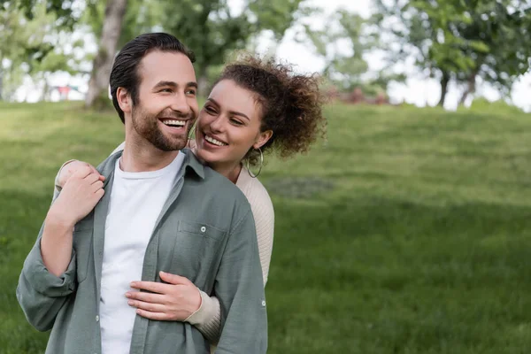 Pleased Curly Woman Hugging Boyfriend Green Summer Park — Stockfoto