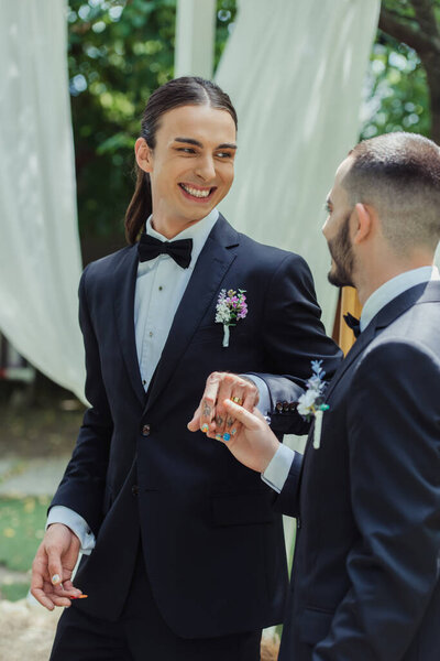 cheerful tattooed gay man with wedding ring holding hands with husband