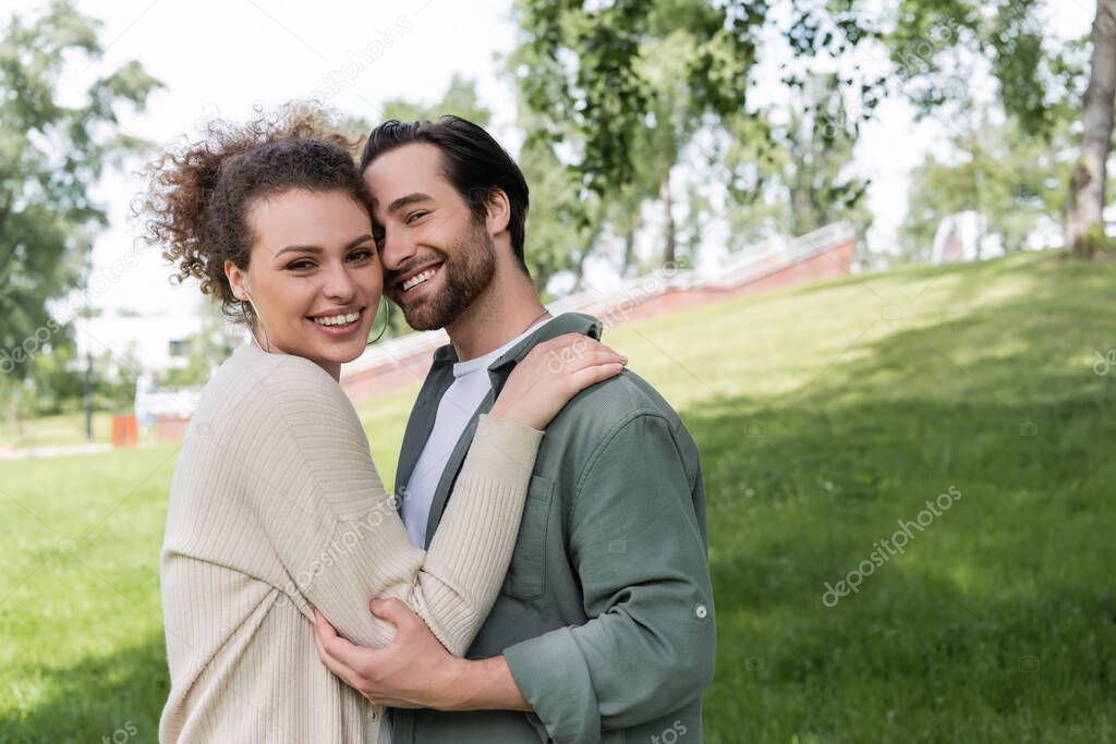 happy bearded man hugging with curly and joyful woman in green summer park 