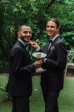 pleased gay newlyweds in formal wear holding wedding cake 