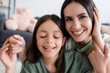 portrait of smiling woman and happy kid with closed eyes smiling at home
