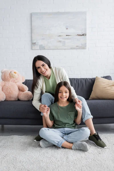 Happy Brunette Babysitter Sitting Sofa Holding Hands Cheerful Girl — Zdjęcie stockowe