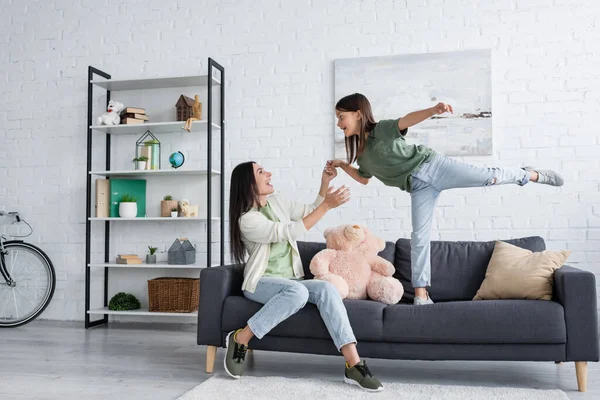 Happy Babysitter Supporting Excited Kid Standing One Leg Couch Living — Zdjęcie stockowe