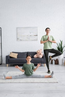 Tam boy dadı ve gözleri kapalı kız oturma odasında yoga pozisyonunda meditasyon yapıyorlar.