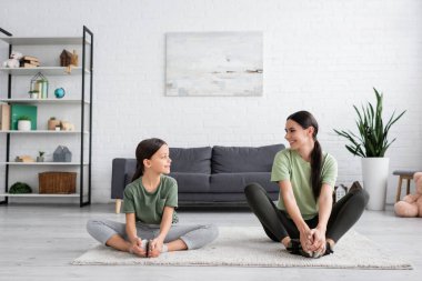 girl and babysitter smiling at each other while sitting on carpet in fire log pose
