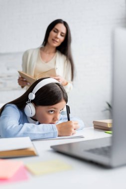 Çevrimiçi ders sırasında kulaklıklı bir kızın yanında kitap yazan bulanık bir bebek bakıcısı.