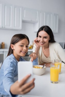 Mutlu kız kahvaltıda bulanık cep telefonunu bakıcısına gösteriyor.
