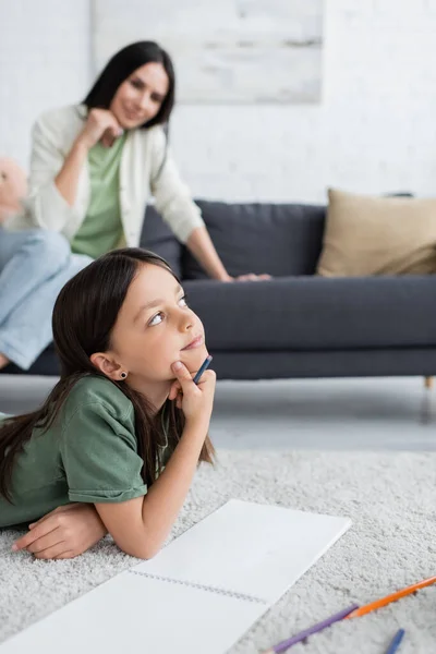 Dreamy Girl Lying Carpet Thinking Blurred Nanny Sitting Sofa — Stockfoto