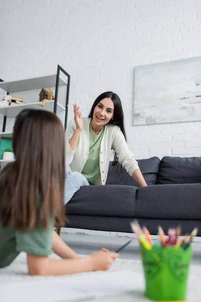 Cheerful Nanny Sitting Sofa Talking Girl Lying Carpet Blurred Colorful — Stock Fotó