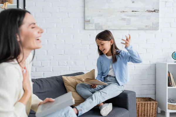 Cheerful Girl Gesturing While Reading Book Nanny Laughing Blurred Foreground — Stockfoto