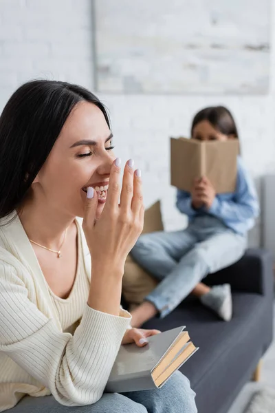 Laughing Nanny Covering Mouth Hand Child Reading Book Blurred Background — Stock fotografie