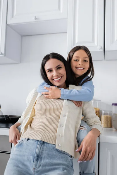 Cheerful Girl Hugging Happy Nanny Smiling Camera Kitchen — Stockfoto