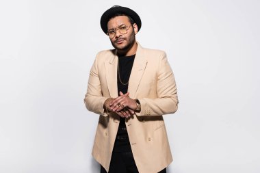 Fötr şapkalı şık Hintli hip hop sanatçısı gri kameraya bakarken poz veriyor.