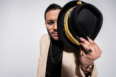 eastern hip hop performer covering half of face with fedora hat isolated on grey