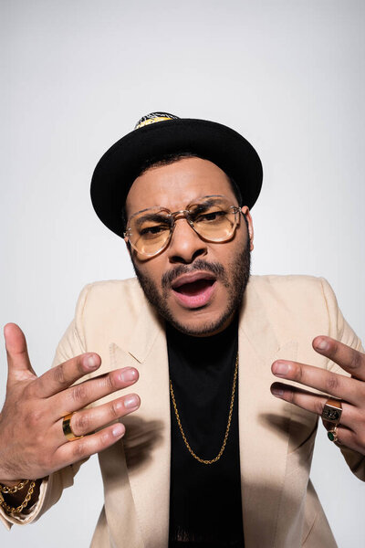 eastern hip hop performer in eyeglasses singing while gesturing isolated on grey