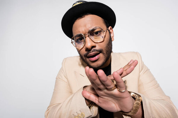 eastern hip hop performer in fedora hat and eyeglasses showing stop gesture isolated on grey