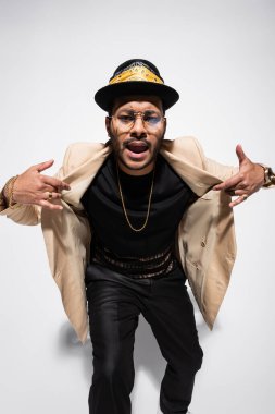 Doğu hip hop sanatçısı fötr şapkalı ve gözlüklü, şarkı söylerken el kol hareketi yapıyor.