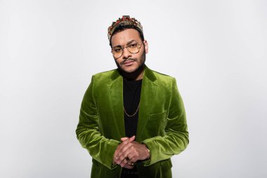 indian hip hop performer in green velvet blazer and crown standing with clenched hands isolated on grey