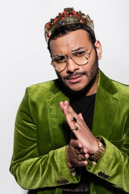 eastern hip hop performer in green velvet blazer and crown on head looking at camera isolated on grey