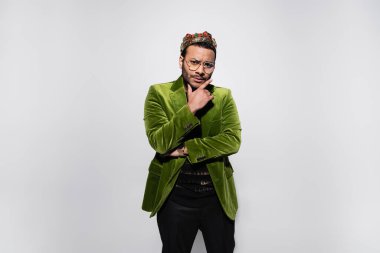pensive eastern hip hop performer in green velvet blazer and crown isolated on grey