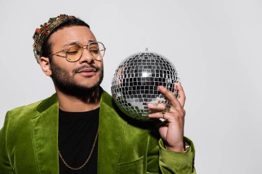 eastern hip hop performer in green velvet blazer and crown holding disco ball isolated on grey