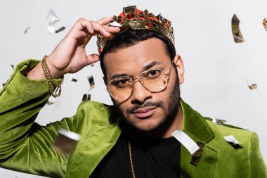 Yeşil kadife ceketli Hintli hip hop sanatçısının portresi ve gri üzerine düşen konfetiye yakın bir taç.