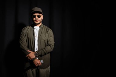 Doğu hip hop sanatçısı, güneş gözlüklü, elinde siyah mikrofon var.