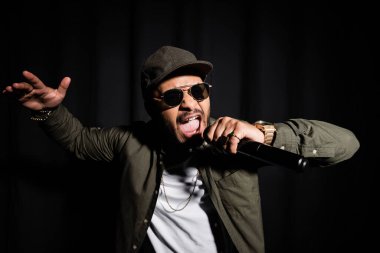 Doğu hip hop şarkıcısı güneş gözlüklü mikrofonda şarkı söylüyor.