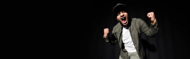 emotional and stylish indian hip hop singer in cap singing loud on black, banner