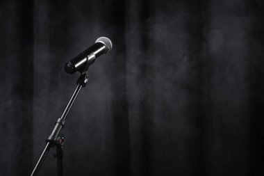 microphone on stand on black stage with curtain and smoke