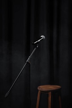 mikrofon siyah sahnede, perde ve tahta sandalyeyle.